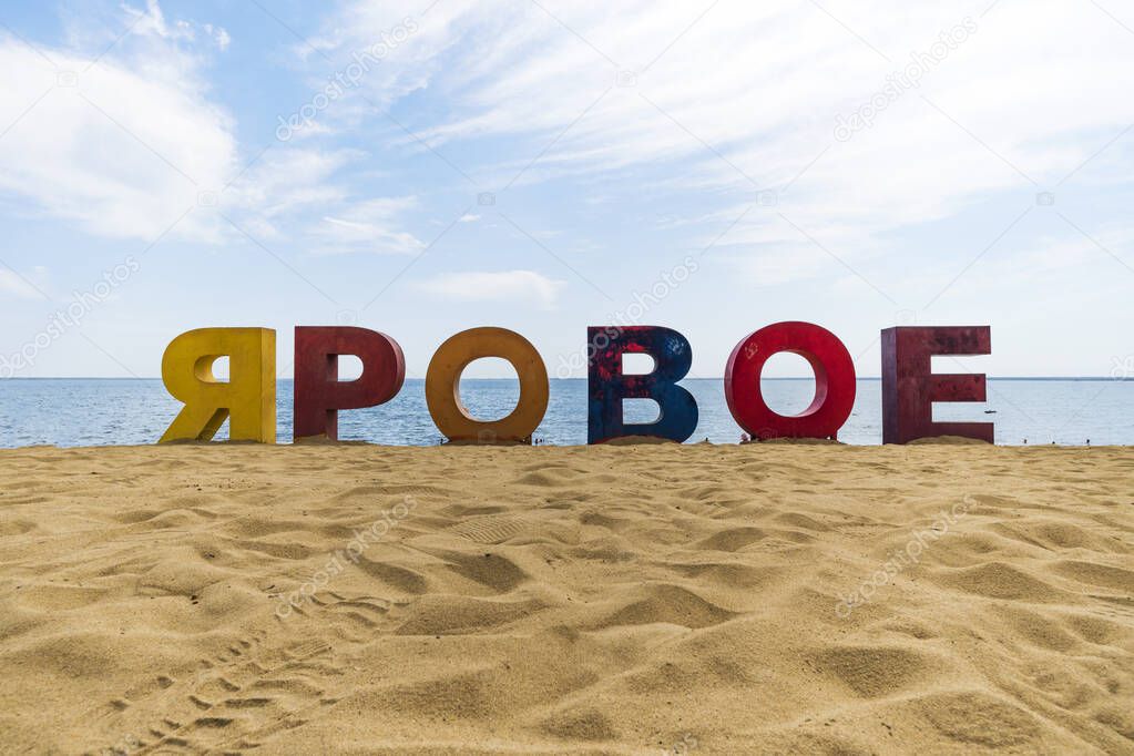 multicolored inscription Yarovoe in russian language on the yellow sand on background of the lake and tourists. Yarovoe name of the resort town in the Altai territory. Russia.