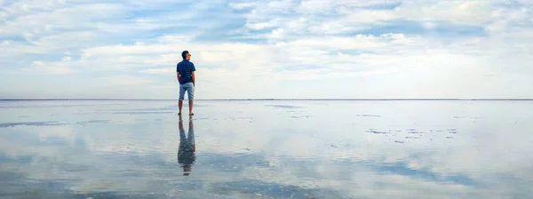 바다의 물 속에 빠진 사람. 행복 한 휴일 과 자유에 대한 개념. 수평선을 보고 있는 관광객. 소금 호수의 아름다운 파노라마와 송로에 하얀 구름 이 반사되어 있는 모습. — 스톡 사진
