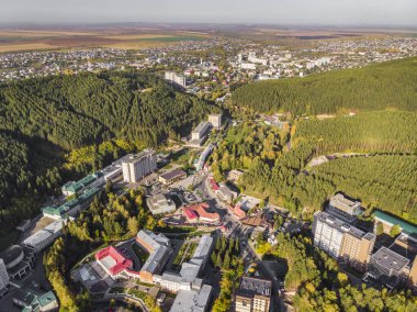 Altai bölgesindeki küçük bir kasabanın havadan görünüşü. Belokurikha tatil köyünün en iyi manzarası. Dağların yamaçlarındaki ormanların arasındaki evlerin kuş bakışı görüntüsü..