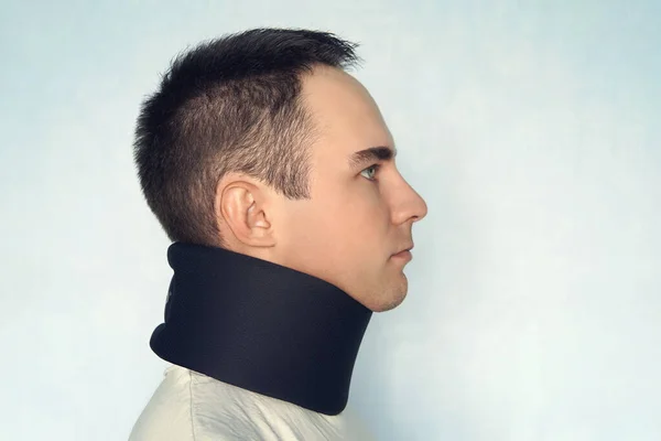Een man met een slechte nek in een zwarte halsband om de halswervels te stabiliseren. Een man met een nekletsel op een blauwe achtergrond. wervelfractuur. Jongeman met halskraag op blauwe achtergrond — Stockfoto