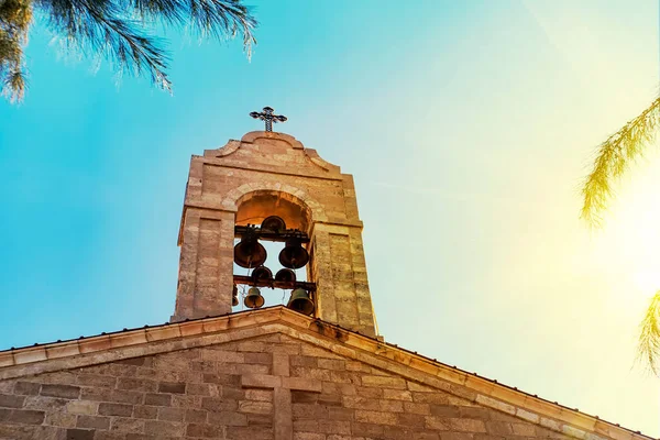 Kirchturm auf dem Dach der christlich-orthodoxen byzantinischen griechischen Kirche. Große Bronzeglocke und ein großes weißes Kreuz, Hintergrundansicht des blauen bewölkten Himmels in leuchtend gelber Sonne — Stockfoto