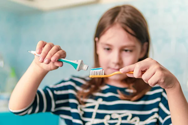 Una bambina di aspetto caucasico lavarsi i denti con uno spazzolino da denti, procedure igieniche al mattino in bagno. — Foto Stock