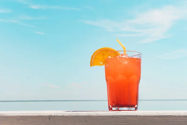 木製のテーブルの上にオレンジジュースのガラスが立っている 青い海を背景にカクテル 喜びの概念 氷のキューブと冷たいさわやかな飲み物 — ストック写真