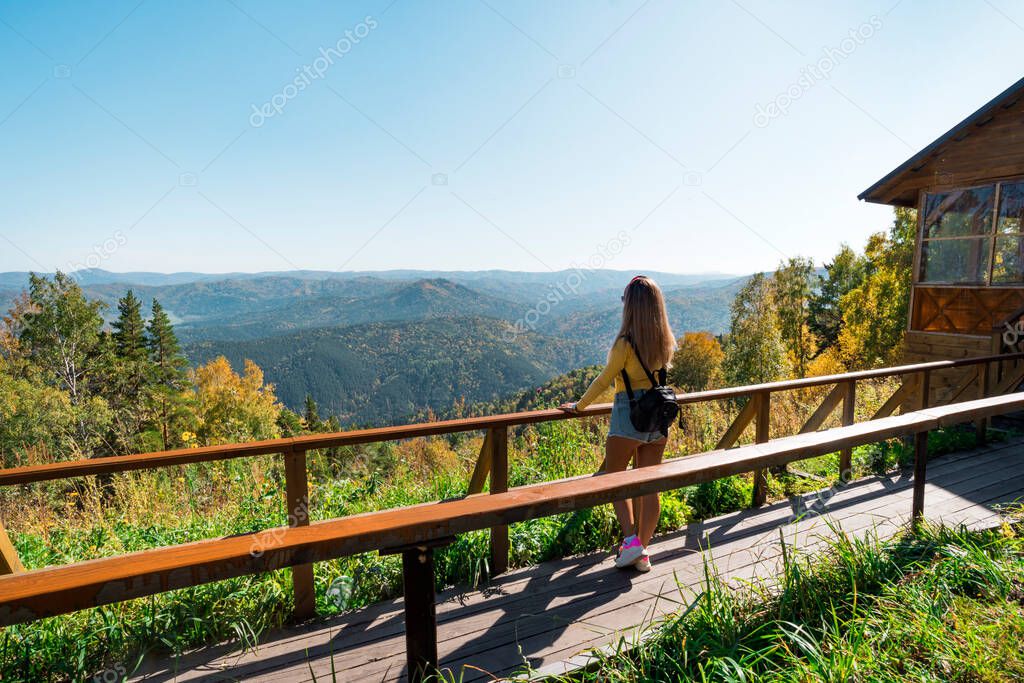 A tourist girl stands on the slope of the mountain Church and looks down on the resort town of Belokurikha. Altai Krai, Russia. Young sexy woman admiring the beautiful views of nature on mountain.