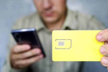 Adamın biri elinde sarı bir SIM kart ve cep telefonu tutuyor. Tasarım ve metin için boş alan