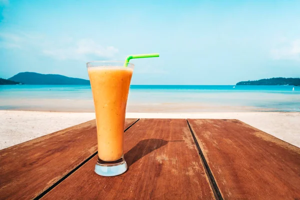 木製のテーブルの上にオレンジジュースのガラスが立っている 青い海を背景にカクテル 喜びの概念 無人のビーチを背景にしたフルーツシェイク — ストック写真