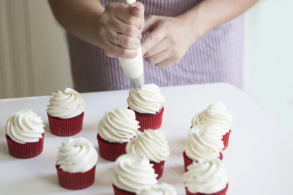 Young girl prepares cupcakes. Close up hands of the chef with confectionery bag squeezing cream on cupcakes. The concept of home cooking