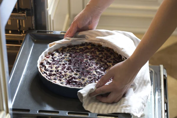 Woman cooking in the kitchen, puts cakes in the oven. Clafoutis cherry pie. preparation of a French pie with cherries