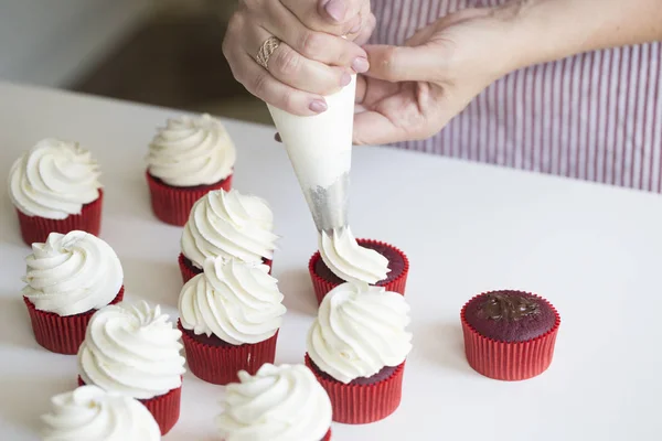 Young girl prepares cupcakes. Close up hands of the chef with confectionery bag squeezing cream on cupcakes. The concept of home cooking