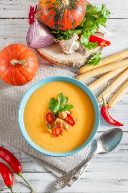 Biber biber, kabak çekirdeği, kruton ve maydanoz Beyaz ahşap zemin üzerinde mavi kase kabak çorbası