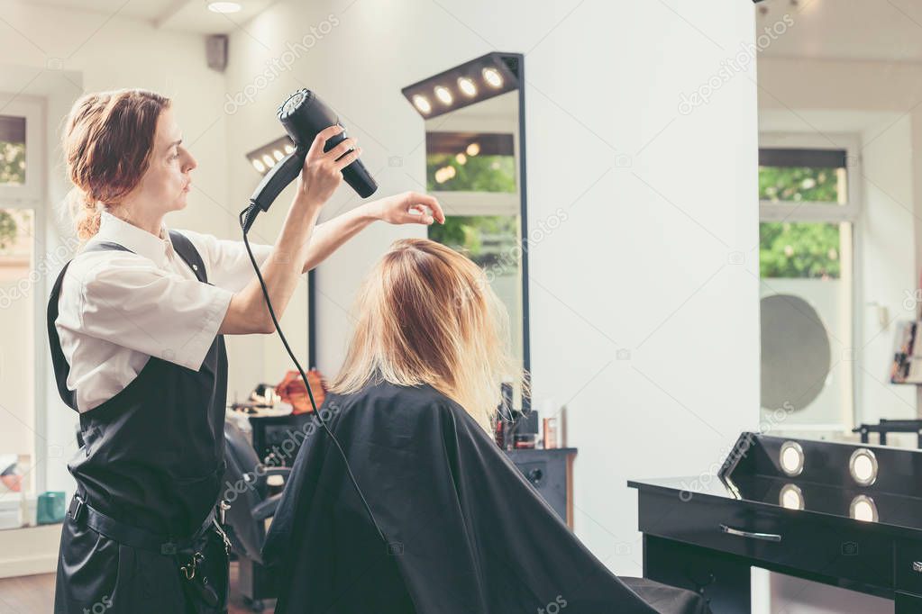 Beautician blow drying woman's hair at beauty salon