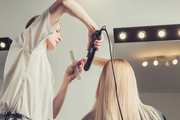 髪は美容院で矯正します ヘアー アイロンを使用するクライアントの髪型を作る美容師 — ストック写真