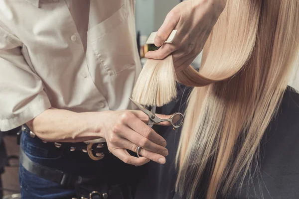 Hairdresser is cutting long blond hair in hair salon