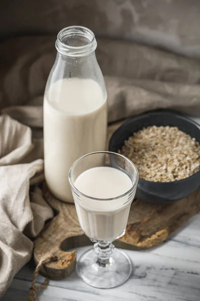 Non dairy oat milk for vegan diet. Oat flakes in a bowl and glass bottle of milk on rustic background
