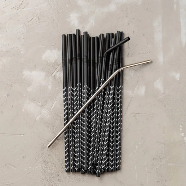 One reusable metal straw against the heap of plastic disposable drinking straws. Zero waste concept