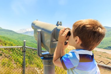 Küçük çocuk, Washington eyaletindeki St. Helens Dağı 'nın zirvesini görmek için teleskop kullanıyor.