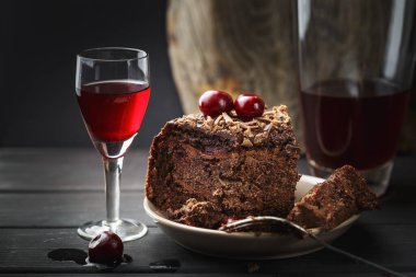 Bir bardak vişneli likör ve arka planda ev yapımı çikolatalı pasta.