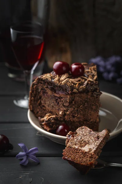 A piece of chocolate cake on a fork cut from a bigger slice. A glass of cherry liquor on the background. Selective focus