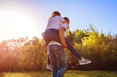 Mutlu genç çift aşık bahar ormanda eğleniyor. Adam kız arkadaşı günbatımında sırtına biniyor. Çocuklar dışarıda soğutma