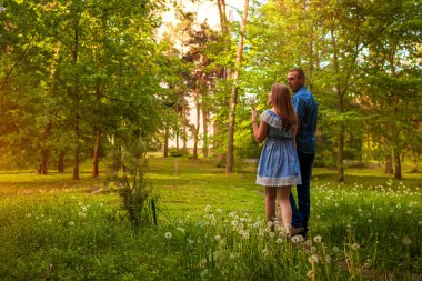Kaç bahar ormanda yürüyüş. Genç adam ve kadın karahindiba günbatımında üfleme. İnsanlar doğanın keyfini