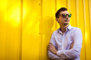 Beyaz gömlek ve sarı duvara karşı açık havada duran güneş gözlükleri şık gencin kapatın. Yaz moda kıyafet.