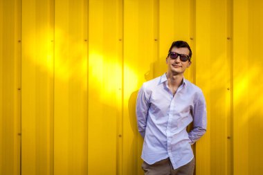 Genç yakışıklı giyen şık yaz outfir sarı duvar açık havada karşı adam. Hippi erkek güneş gözlüğü