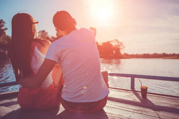 恋川の上を抱いて幸せなカップルは 日没時ドックします 景色を楽しみながら水で低温の若者 — ストック写真