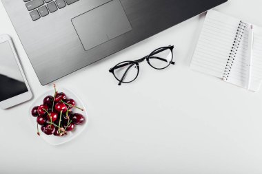 Üstten görünüm serbest meslek Danışma tablo dizüstü bilgisayar, dizüstü bilgisayar, smartphone, gözlük ve aperatif. Kiraz çalışırken sahip. Çalışma alanı.