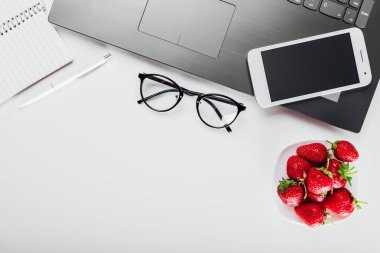 Üstten görünüm office çalışanın dizüstü bilgisayar, dizüstü bilgisayar, smartphone, gözlük ve sağlıklı snack. Çilek çalışırken sahip.