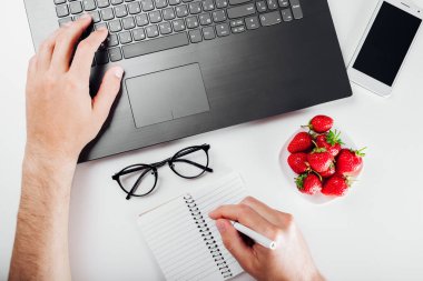 Üstten görünüm Freelancer dizüstü bilgisayar, dizüstü bilgisayar, smartphone, gözlük ve aperatif. Evden çalışan. Adam notlar