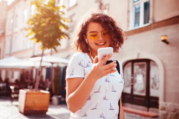 Güzel genç kız akıllı telefon kullanarak ve sokakta yürürken müzik dinlemek. Mutlu kadın dans ve having fun