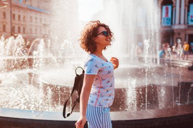 Çeşmenin yaz aylarında yürüyüş sırt çantası ile mutlu genç kadın. Üniversiteli kız açık havada soğutma sonra sınıfları