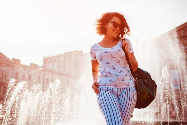 Çeşmenin yaz aylarında yürüyüş sırt çantası ile mutlu genç kadın. Üniversiteli kız açık havada soğutma sonra sınıfları