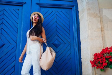 Mavi ahşap kapı karşı gülümseyen mutlu bir genç kadın. Açık şık yaz kıyafeti giymiş güzel üniversiteli kız portresi