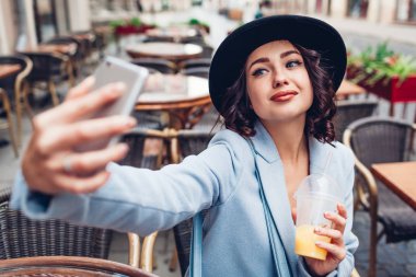 Açık Cafe portakal suyu yaparken selfie alarak güzel ve genç birbayan. Şık moda kız arkadaş için bekleyen sokakta soğutma