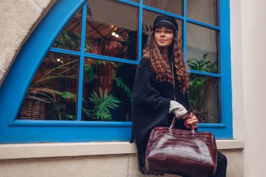 Mavi pencere karşı açık havada poz şık genç kadın. Şık kıyafet. Kıvırcık saçlı gülümseyen güzel model