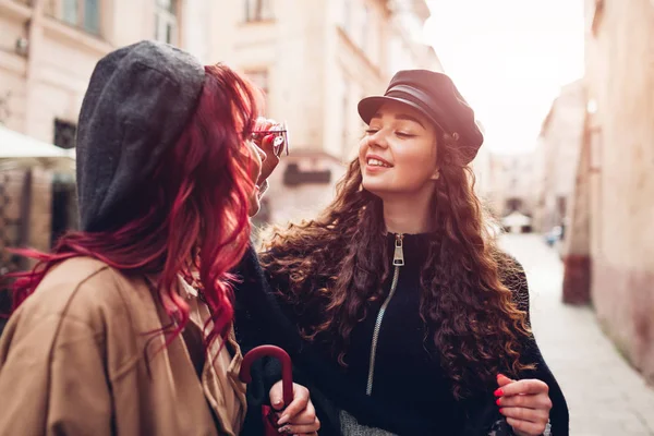 Young women puts glasses on her friend\'s face to try on city street. Friends laughing and having fun
