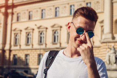 Yakışıklı üniversitelim gözlüklerini üniversite karşı denetleme. Sırt çantası gülümseyen mutlu erkek öğrenci. Eğitim