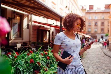 Akıllı telefon ve holding kitap açık havada sonra sınıfları kullanan güzel kolej kız. Şık öğrenci