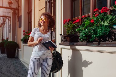 Bir kitap holding ve grup için bekleyen üniversite tarafından müzik dinlemek güzel üniversiteli kız. Sırt çantası gülümseyen mutlu öğrenci
