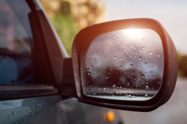 Yan dikiz aynası modern bir araba. Yağmurlu su cam üzerine bırakır. Güneş yansıma.