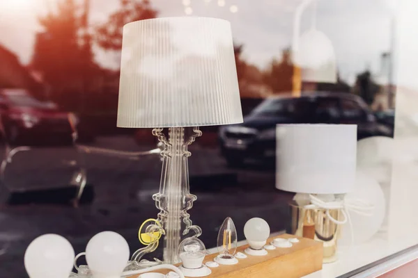 Showcase of lamp store. Contemporary floor lamps, bulbs and chandeliers displayed on window sill