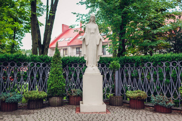 Statue of virgin Mary outdoors. Holy mother statue located in summer garden. Religious place to pray on city street. Religion concept