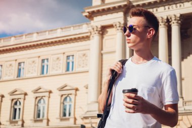 Yakışıklı üniversitelim üniversitenin karşı kahve içme. Adam öğrenci sınıfları sonra rahatlatıcı sırt çantası ile. Yaşam tarzı