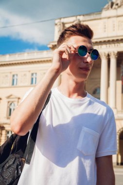 Yakışıklı üniversitelim gözlüklerini üniversite karşı denetleme. Sırt çantası gülümseyen mutlu erkek öğrenci. Eğitim