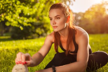 Genç sportif kadın yaz Park yapıyor. Çimenlerin üzerinde otururken bacaklarını germe sporcumuz. Spor kavramı