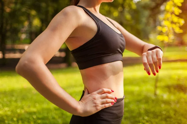 Sports watch. Runner checking burned calories. Woman looking at watch in summer park. Closeup of female hand