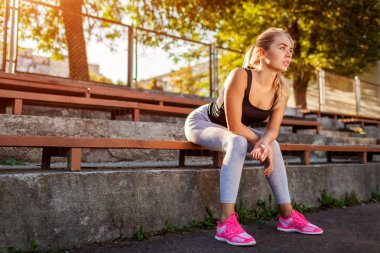 Genç kadın atlet sportsground üzerinde yaz aylarında çalıştırdıktan sonra dinlenme. Sportif erkek egzersiz yaptıktan sonra bankta oturan