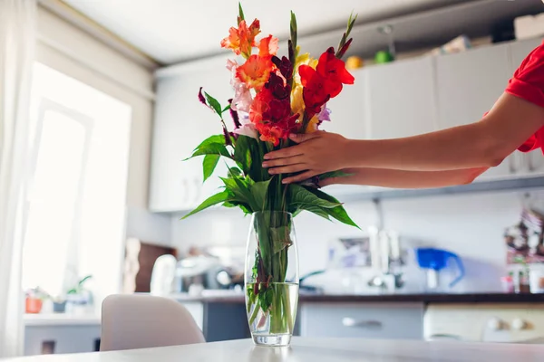 Woman puts red flowers in vase. Young housewife taking care of coziness in kitchen. Modern kitchen design. White and silver kitchen