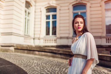 Açık havada beyaz gelinlik giyen güzel kadın. Tek omuzlu elbise aksesuarları ve mücevher. Moda. Şık makyaj